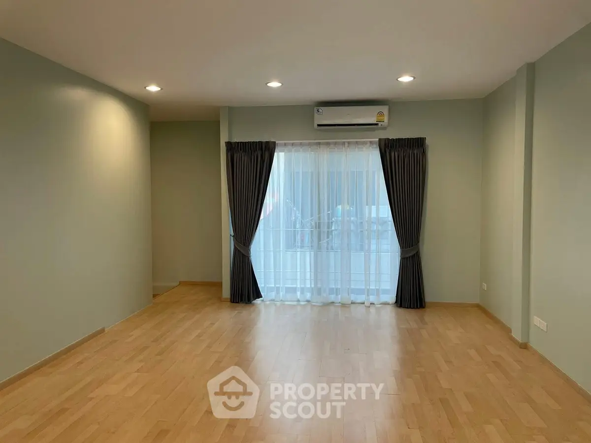 Spacious empty living room with wooden flooring and large window with curtains.
