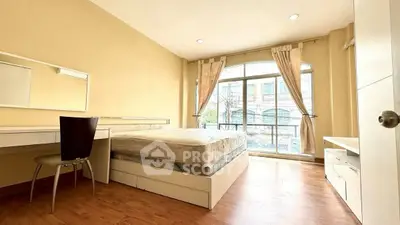 Bright bedroom with large window and wooden flooring, featuring a cozy bed and study desk.