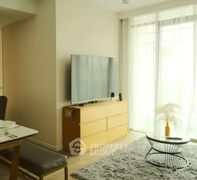 Modern living room with sleek TV, stylish furniture, and natural light from large windows.