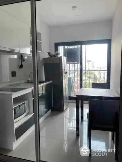 Modern kitchen with sleek white cabinetry and high-gloss floor tiles opens onto a sunlit balcony with urban views, perfect for city living.