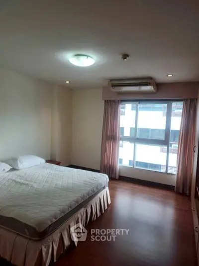 Spacious bedroom with large window and wooden flooring in modern apartment.