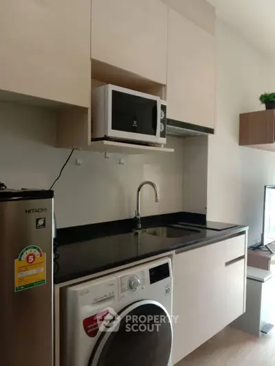 Modern kitchen with sleek appliances including fridge, microwave, and washing machine in compact layout.