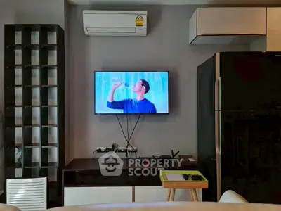 Modern living room with wall-mounted TV, air conditioning, and sleek black refrigerator.