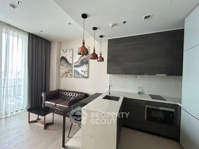 Modern living room with open kitchen, featuring stylish pendant lights and a cozy leather sofa.