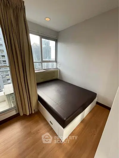 Cozy bedroom with city view, featuring a compact bed and large windows for natural light.