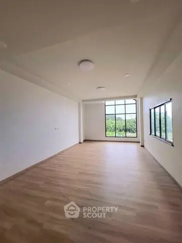 Spacious empty room with large windows and wooden flooring, perfect for customization.