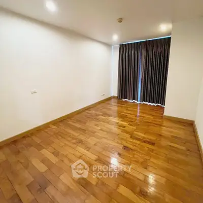 Spacious empty room with wooden flooring and large window, perfect for customization.