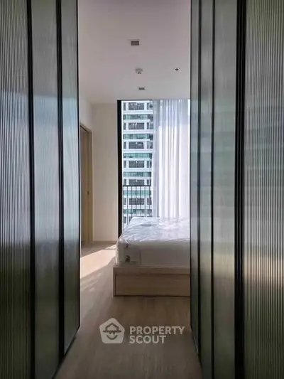 Modern bedroom with floor-to-ceiling windows and city view, featuring sleek design and natural light.