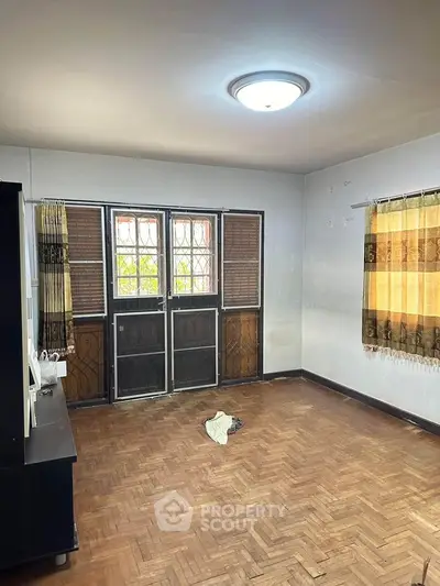 Spacious empty room with parquet flooring and large windows, ideal for customization.