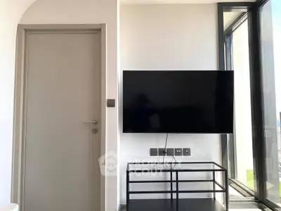 Modern living room with sleek TV setup and large window offering natural light.