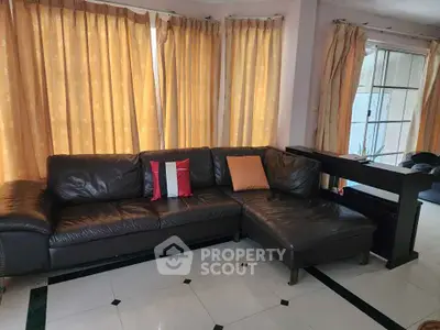 Spacious living room with elegant black leather sectional sofa and large windows with curtains.