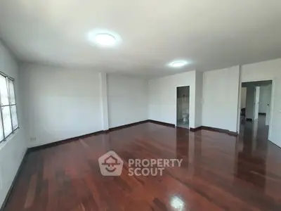 Spacious empty living room with polished wooden floors and bright lighting.