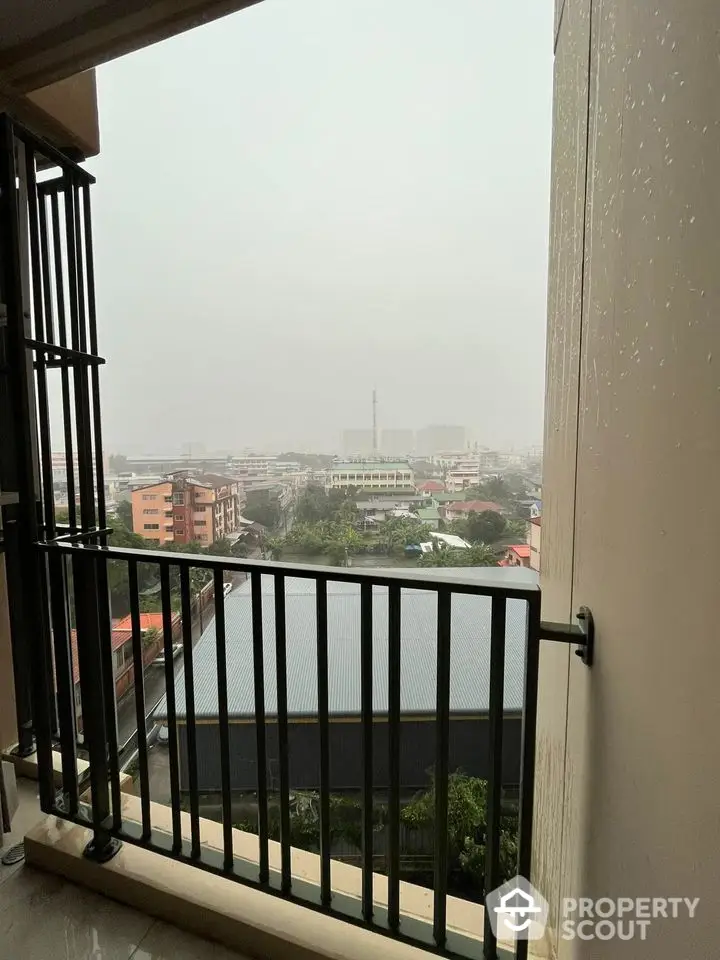 City view from a balcony on a rainy day, showcasing urban landscape and overcast sky.