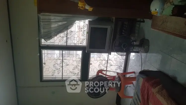 Cozy living room with vintage TV and fan, floral window design, and colorful decor.