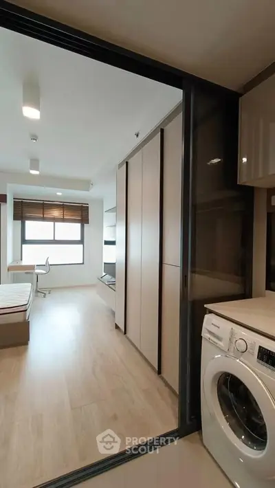 Modern apartment interior with washing machine and spacious bedroom view.