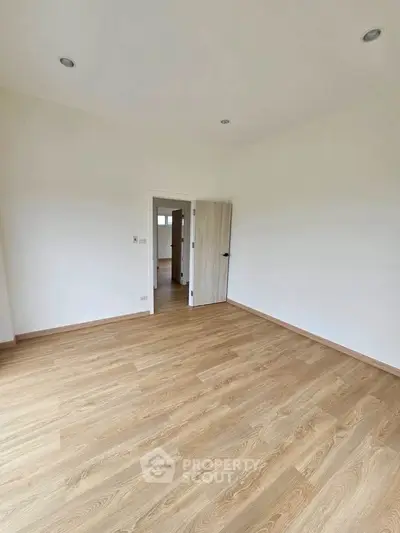 Spacious empty room with wooden flooring and white walls, perfect for customization.