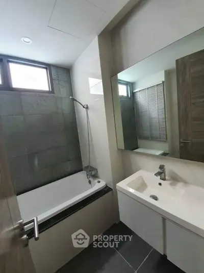 Modern bathroom with sleek design and bathtub, featuring large mirror and contemporary fixtures.
