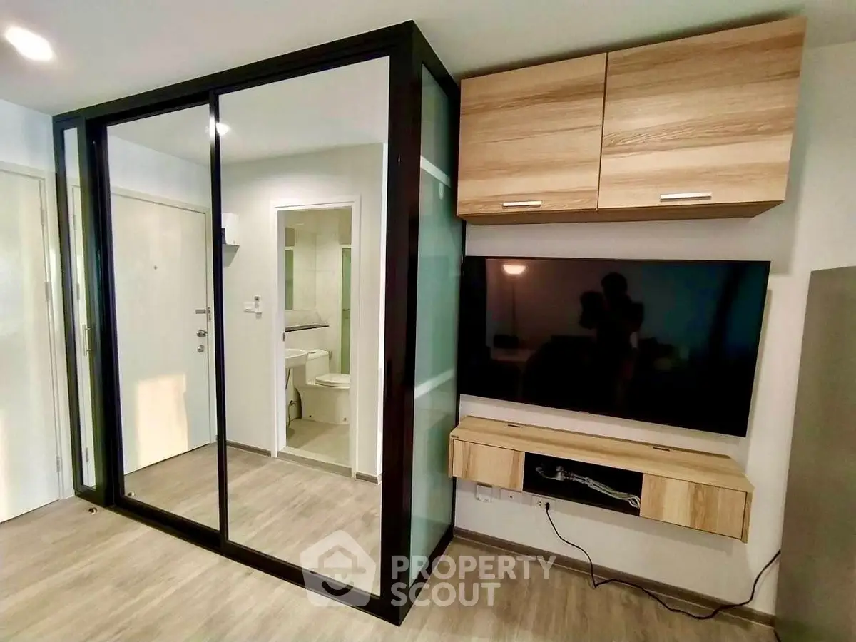 Modern living room with sleek TV setup and glass partition leading to bathroom.