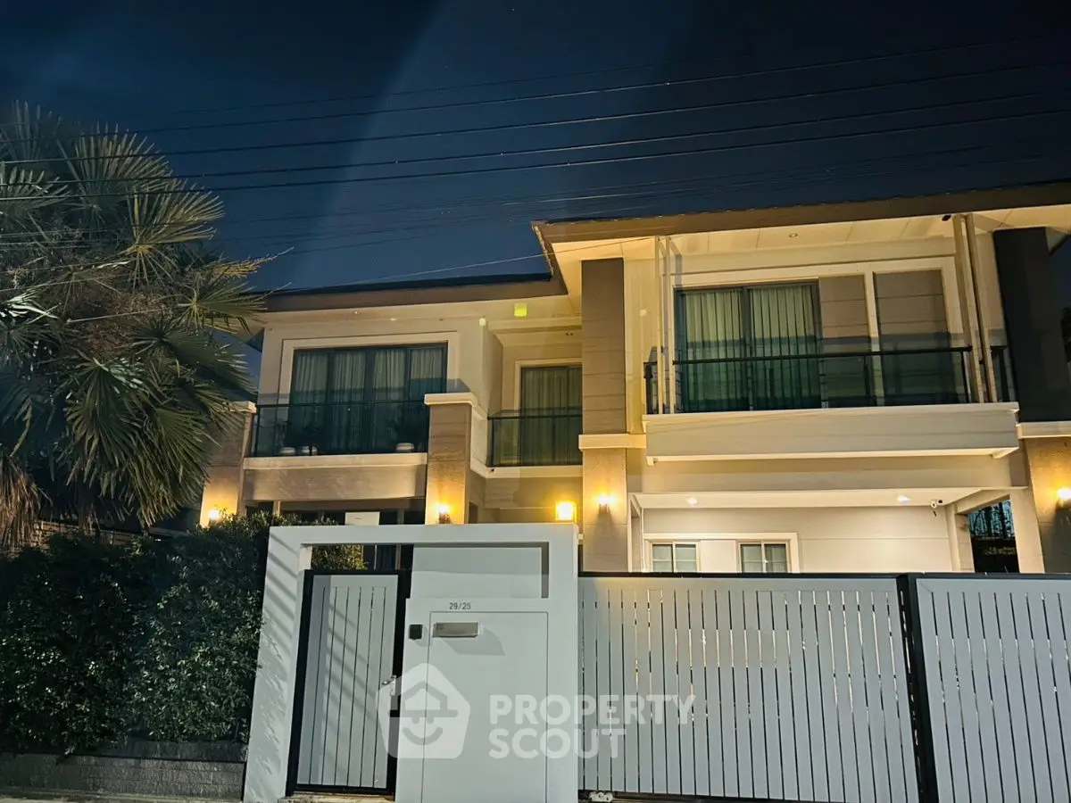 Luxurious modern two-story house with elegant lighting and secure gated entrance at night.