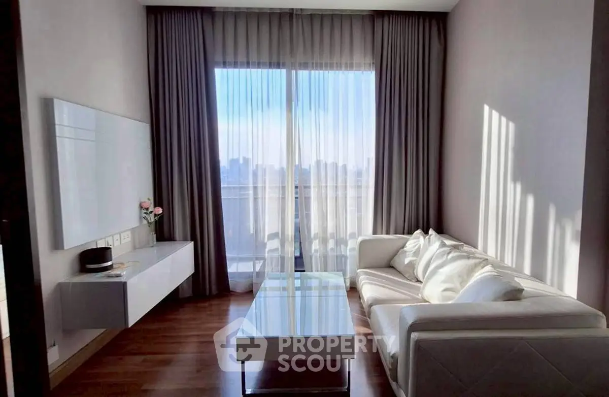 Modern living room with elegant decor and city view, featuring a sleek white sofa and glass coffee table.