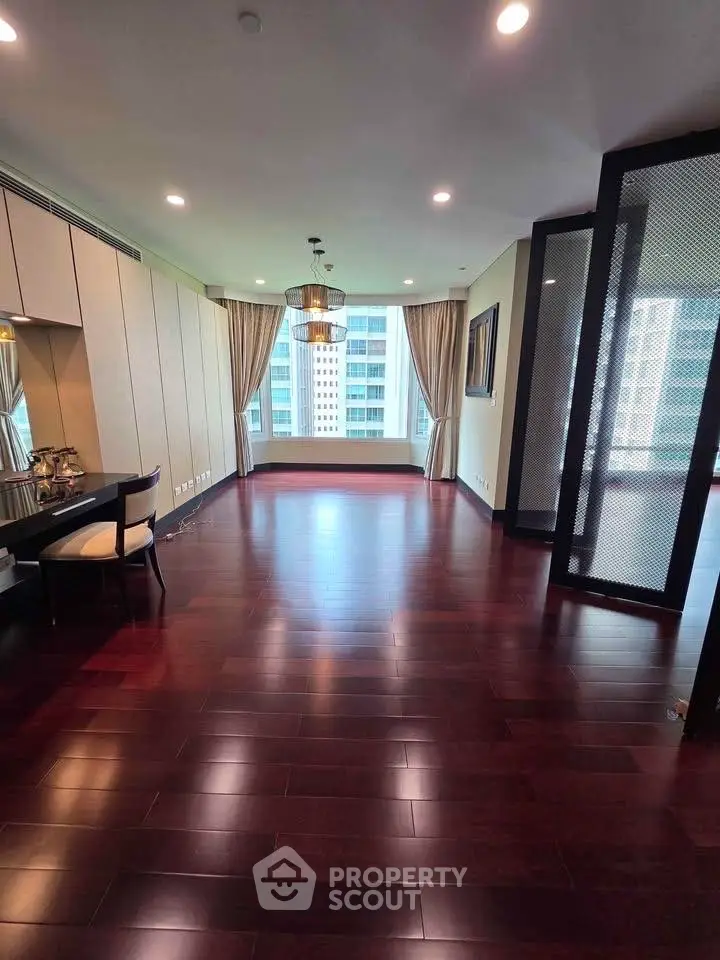 Spacious living room with hardwood floors and large windows offering city views in a modern apartment.