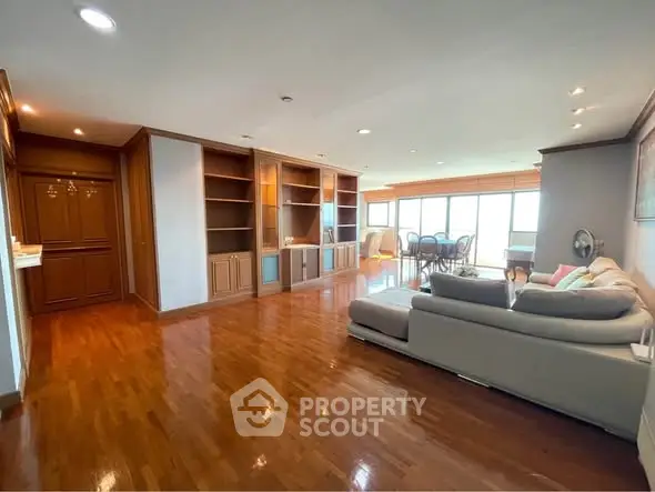 Spacious living room with wooden flooring and built-in shelves, featuring a cozy sofa and dining area with natural light.