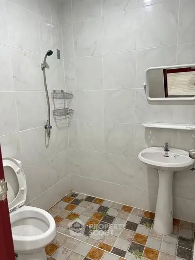 Compact bathroom with tiled walls and floor, featuring a shower, toilet, and pedestal sink.