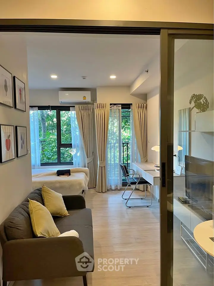 Modern living room with cozy sofa, study desk, and large windows overlooking greenery.