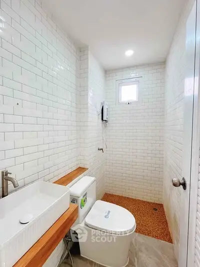 Modern bathroom with white subway tiles and wooden accents, featuring a sleek sink and toilet.