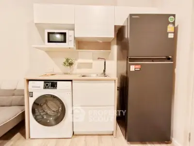 Modern compact kitchen with washing machine, microwave, and fridge in a cozy apartment.