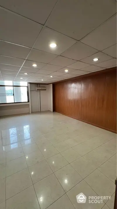 Spacious empty room with tiled flooring and wood panel accent wall