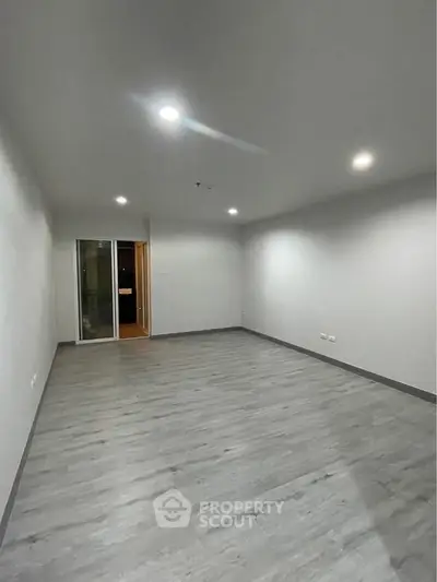 Spacious empty room with modern flooring and recessed lighting, ideal for customization.