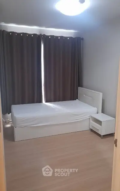 Minimalist bedroom with single bed and nightstand, featuring wooden flooring and dark curtains.