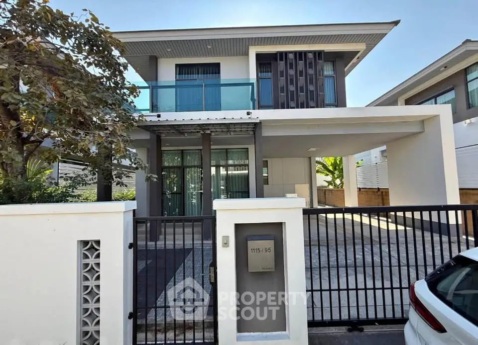Modern two-story house with sleek design and gated driveway in a suburban neighborhood.