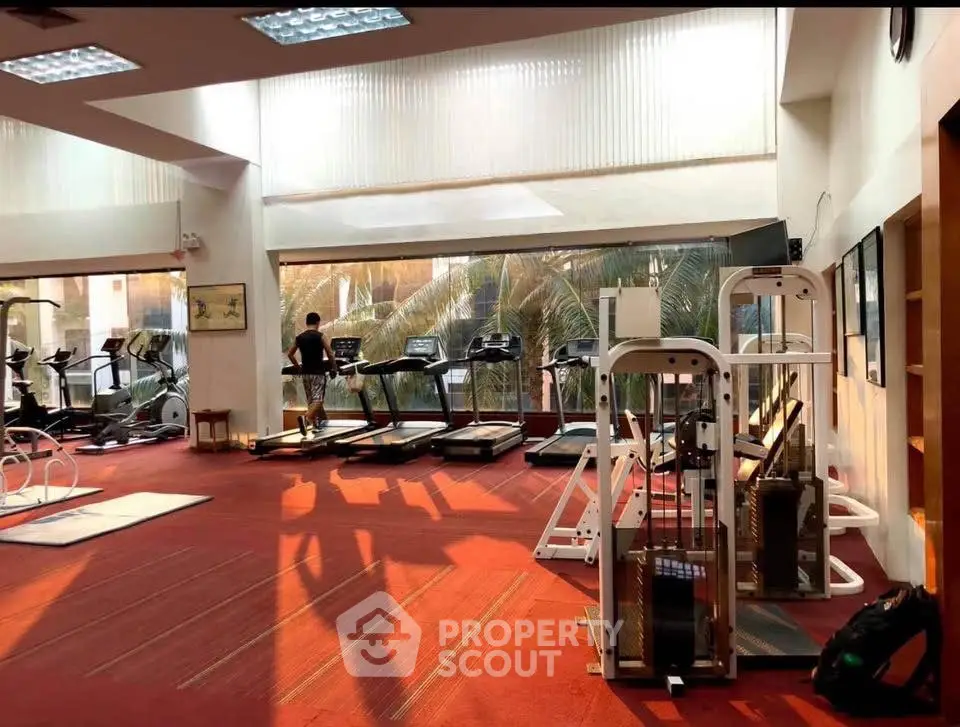 Spacious gym with modern equipment and large windows offering natural light.