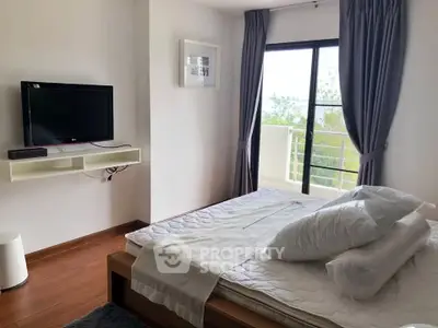 Cozy bedroom with balcony access and modern TV setup in a serene apartment.