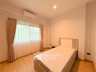 Spacious bedroom with natural light and modern design, featuring a large window and elegant curtains.