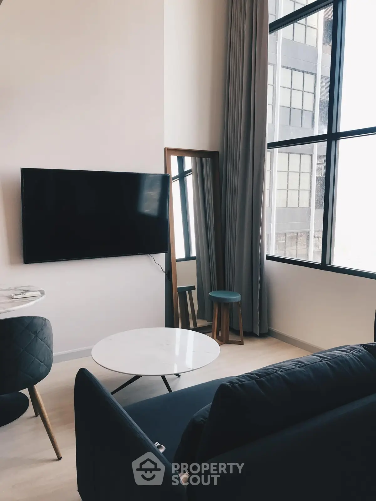 Modern living room with high ceilings and large windows, featuring a sleek black sofa and wall-mounted TV.