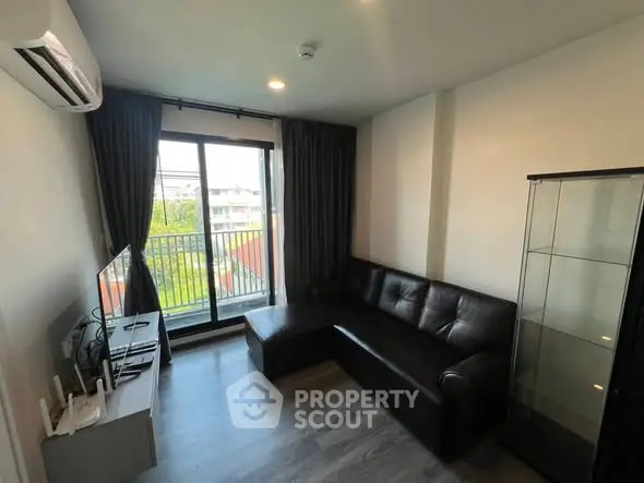 Modern living room with sleek black sofa and large window offering natural light and balcony view.