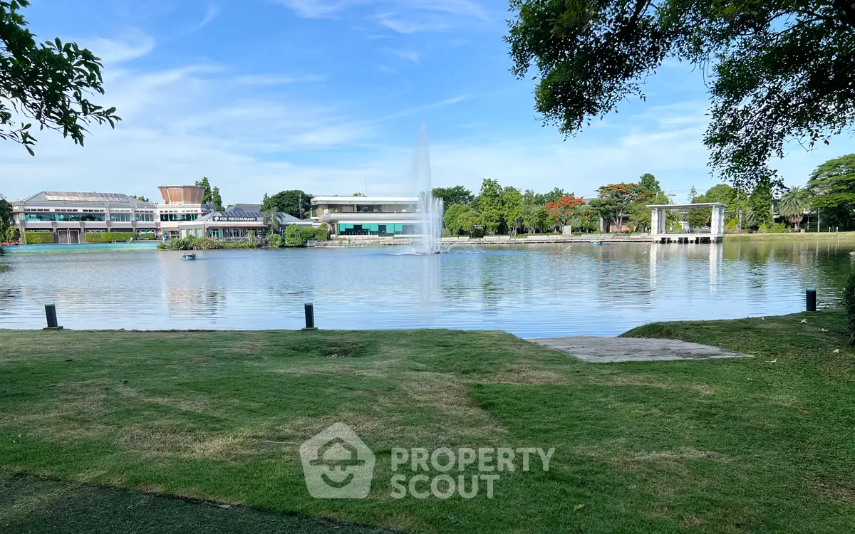 Scenic view of a serene lake with lush greenery and modern buildings in the background, perfect for tranquil living.