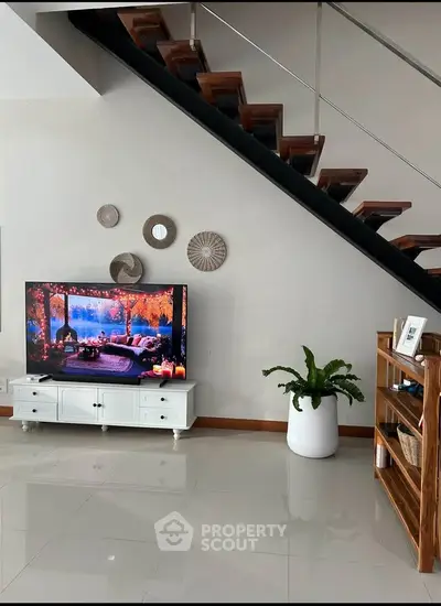 Modern living room with stylish staircase and large TV, featuring elegant decor and glossy tiled flooring.