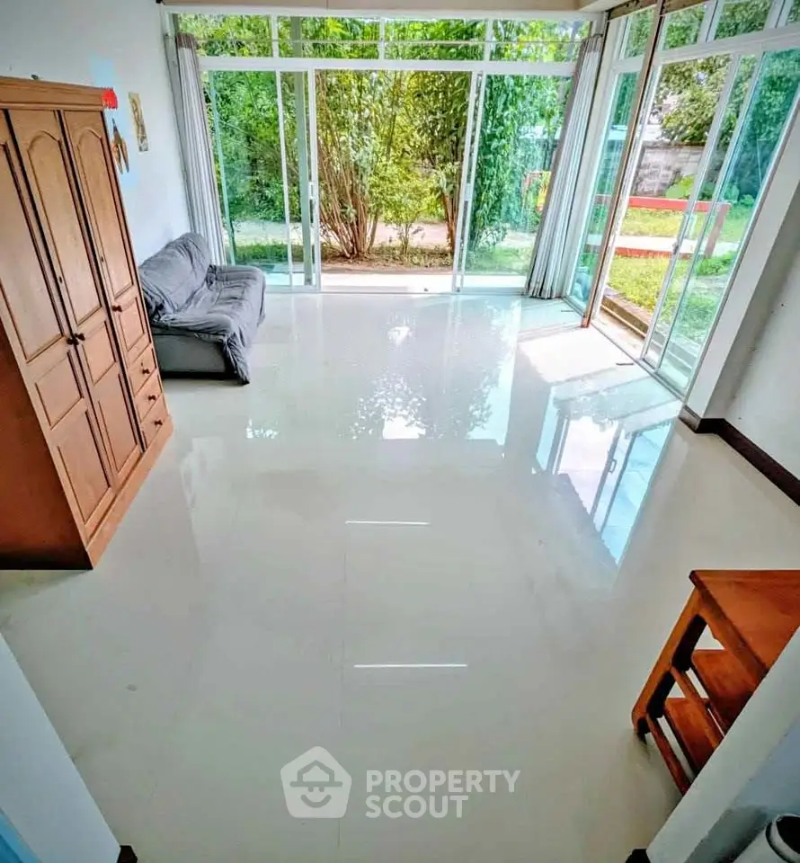 Bright living room with large windows and garden view, featuring a cozy sofa and wooden furniture.