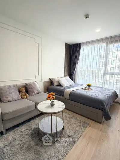 Modern studio apartment with cozy bed and stylish seating area, featuring large windows and elegant decor.