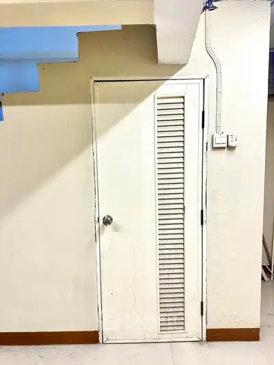 Unique storage space under staircase with white louvered door in modern home.