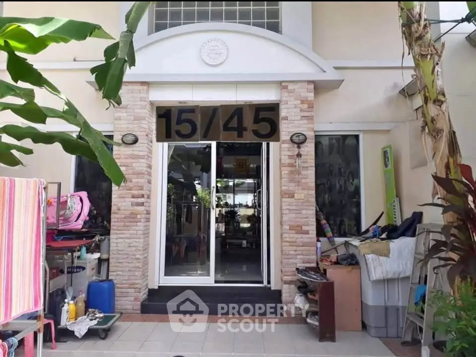 Charming residential entrance with modern glass doors and brick accents, surrounded by lush greenery.