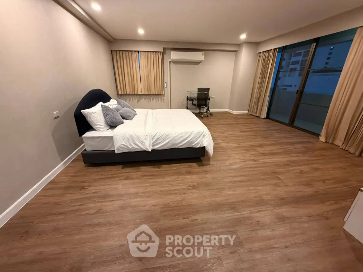 Spacious modern bedroom with wooden flooring and large windows in a luxury apartment.
