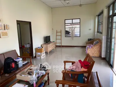Spacious living room with natural light, featuring wooden furniture and tiled flooring, ideal for family gatherings.