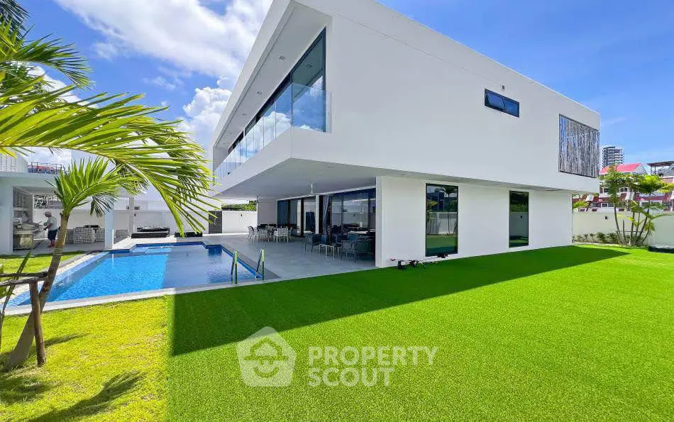 Modern luxury home with pool and lush green lawn under clear blue sky.