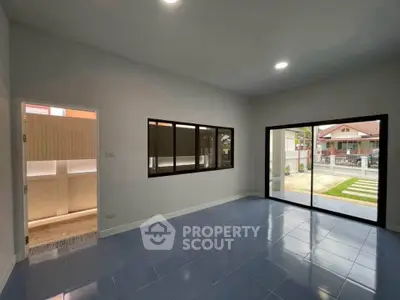 Spacious living room with large windows and blue tiled floor, offering a view of the garden.