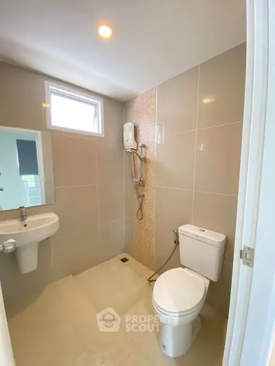 Modern bathroom with sleek fixtures and neutral tiles, featuring a shower and toilet.